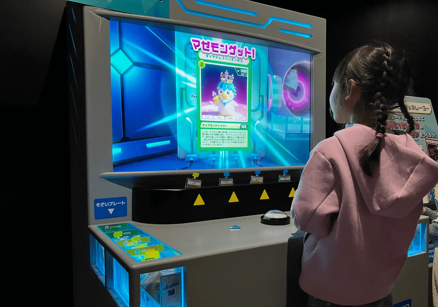 マシンの前でボタンをおす子ども。画面には「マゼモンゲット！」と、生まれたマゼモンのカードが映っている